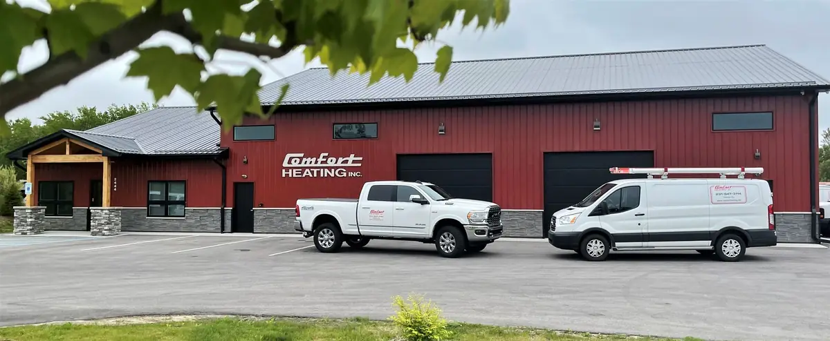 The Comfort Heating Inc shop at 2444 Meadowlands Drive, Traverse City, with the wordmark on the red steel wall and two liveried company vehicles parked outside