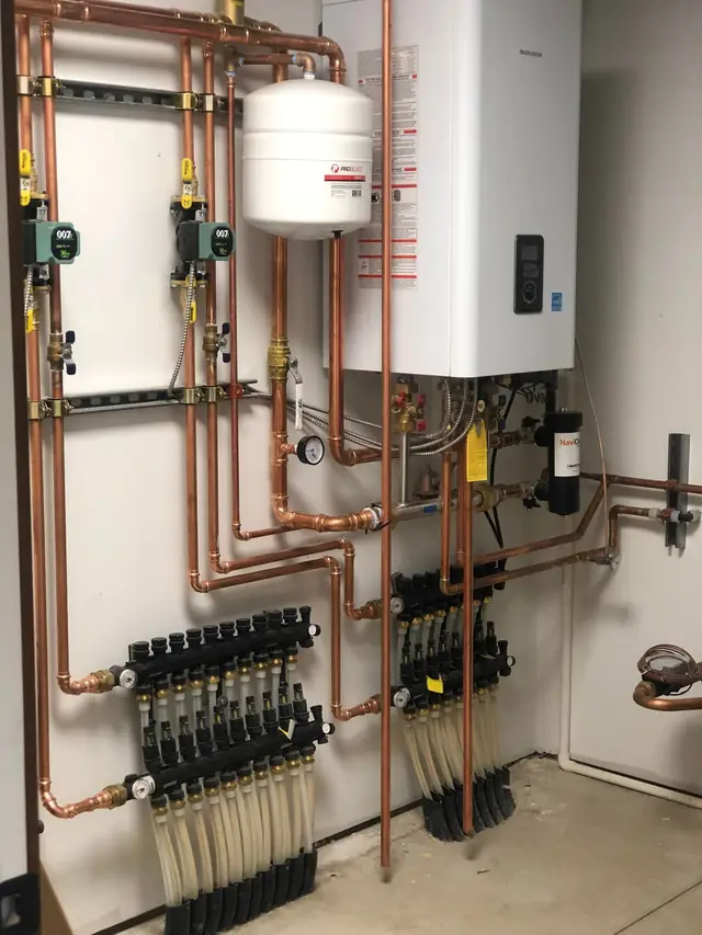 Navien tankless boiler with dual radiant manifolds, flow meters and labelled loops in a finished mechanical room
