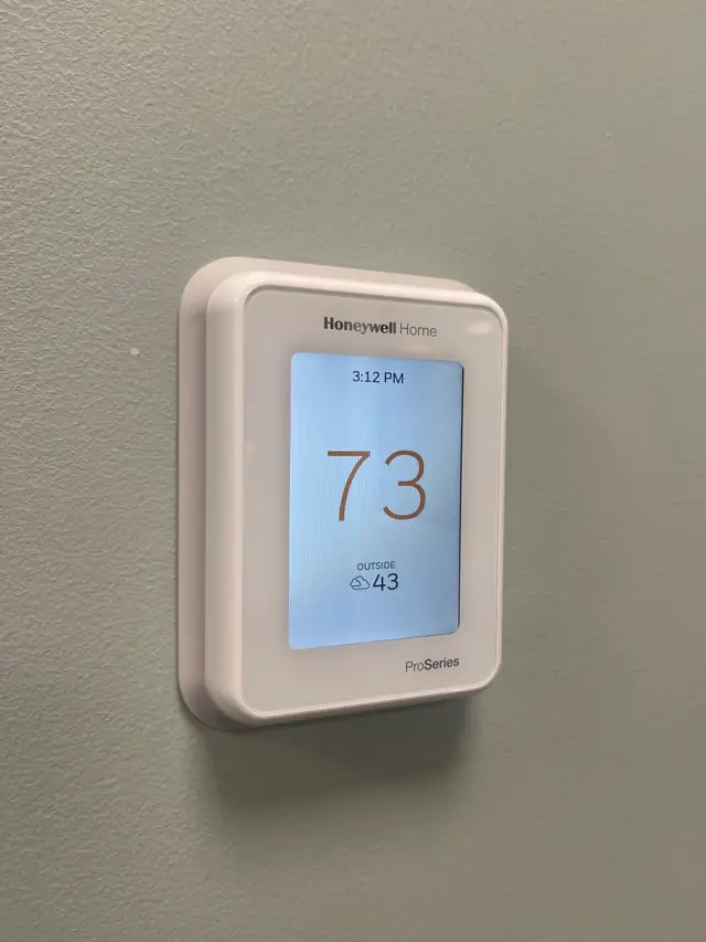 Honeywell Home ProSeries smart thermostat mounted on a wall with the screen lit