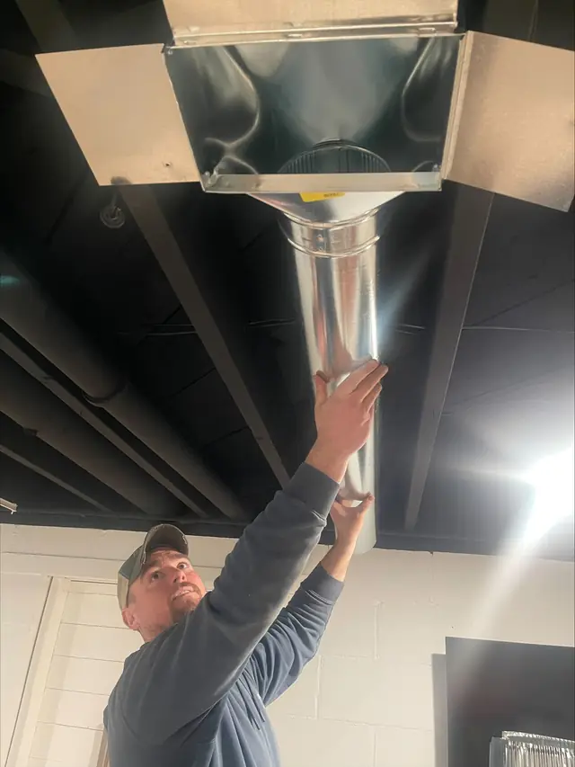 A Comfort Heating technician working on ductwork overhead
